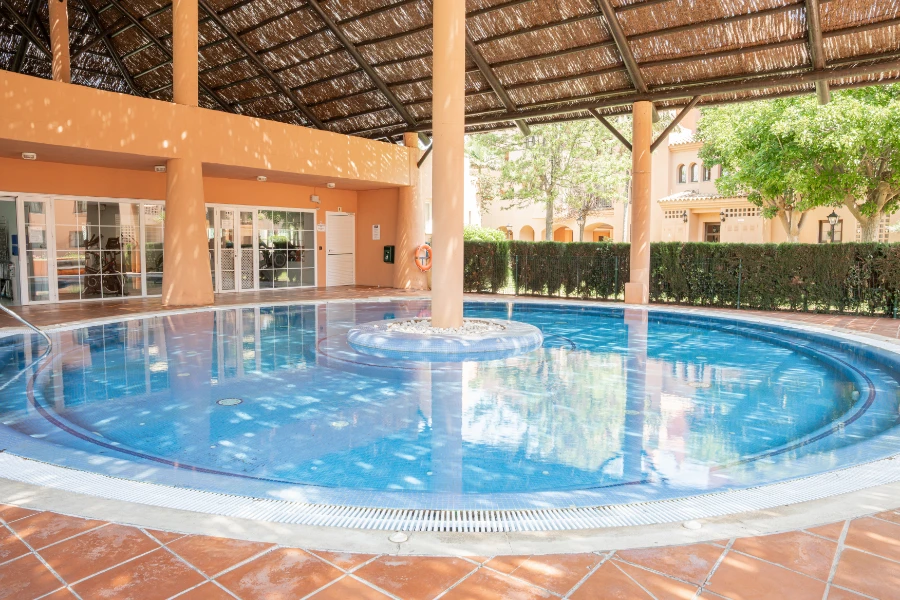 Community swimming pool with shaded area, surrounded by gardens and modern architecture, ideal for relaxation in Marbella.