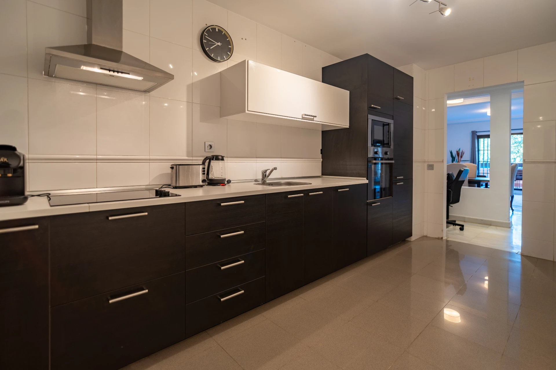 Modern kitchen with dark cabinetry, stainless steel appliances, and a view into a bright living area, showcasing a comfortable vacation rental in Marbella.