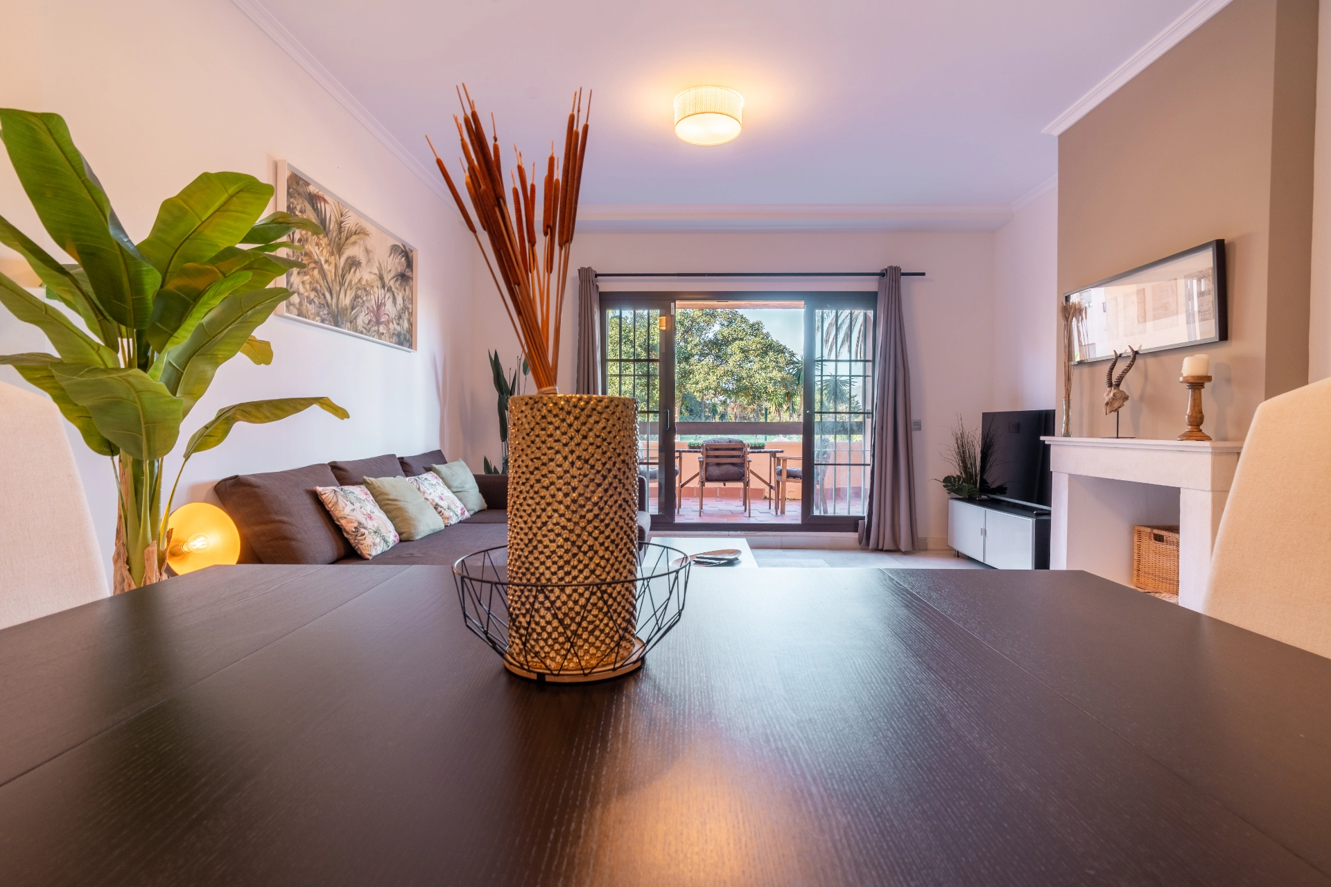Modern living room with cozy seating, decorative pillows, and a view of a terrace, featuring plants and a stylish table, reflecting a comfortable vacation rental in Marbella.
