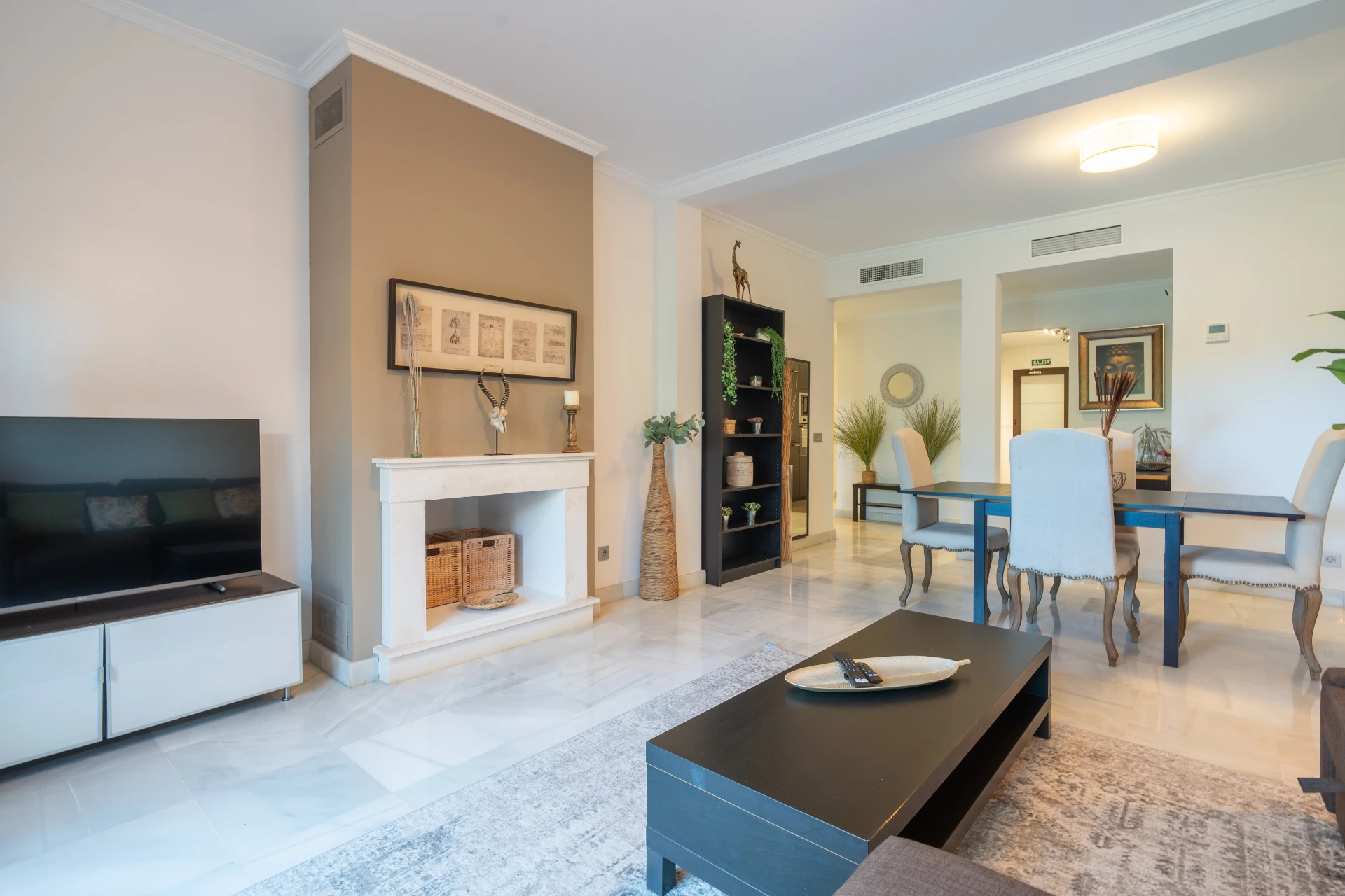 Modern living room featuring a flat-screen TV, elegant fireplace, and stylish dining area, showcasing a comfortable and inviting atmosphere in a Marbella vacation rental.