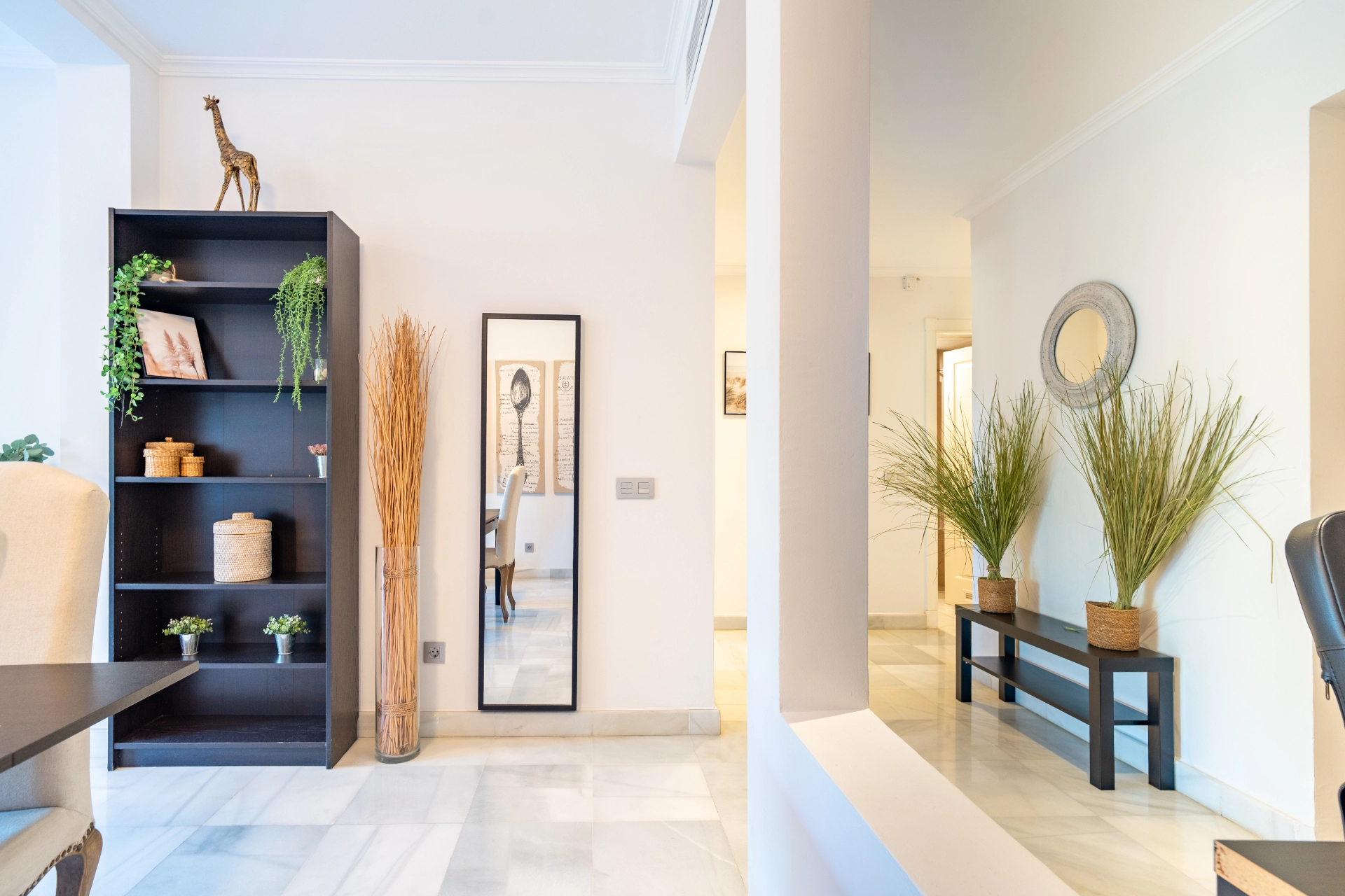 Modern living space featuring a stylish bookshelf with decorative plants, a mirror, and natural accents, showcasing a serene atmosphere ideal for a vacation rental in Marbella.