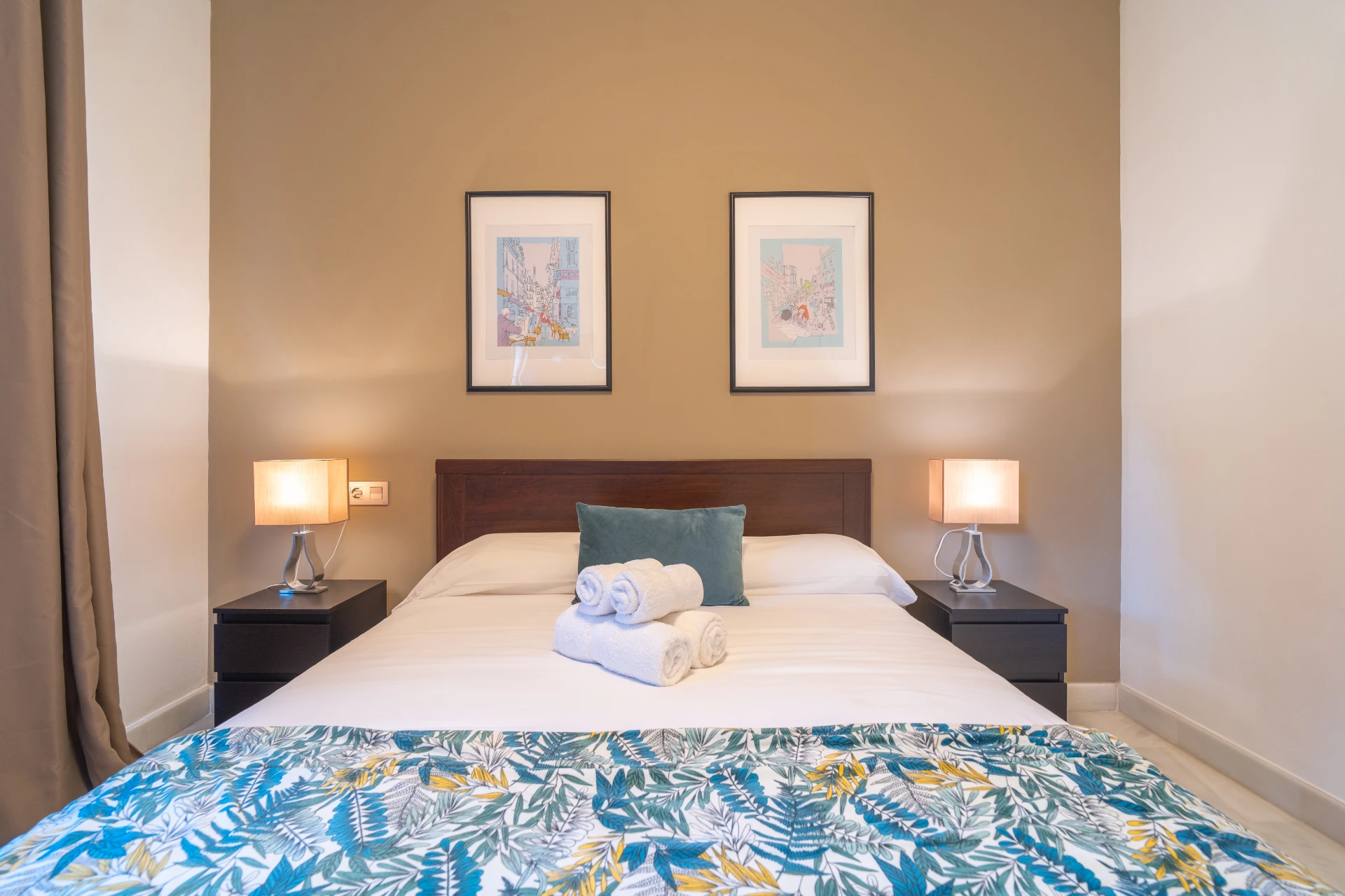 Cozy bedroom featuring a double bed with decorative pillows, fresh towels, bedside lamps, and framed artwork, ideal for a restful stay in Marbella.
