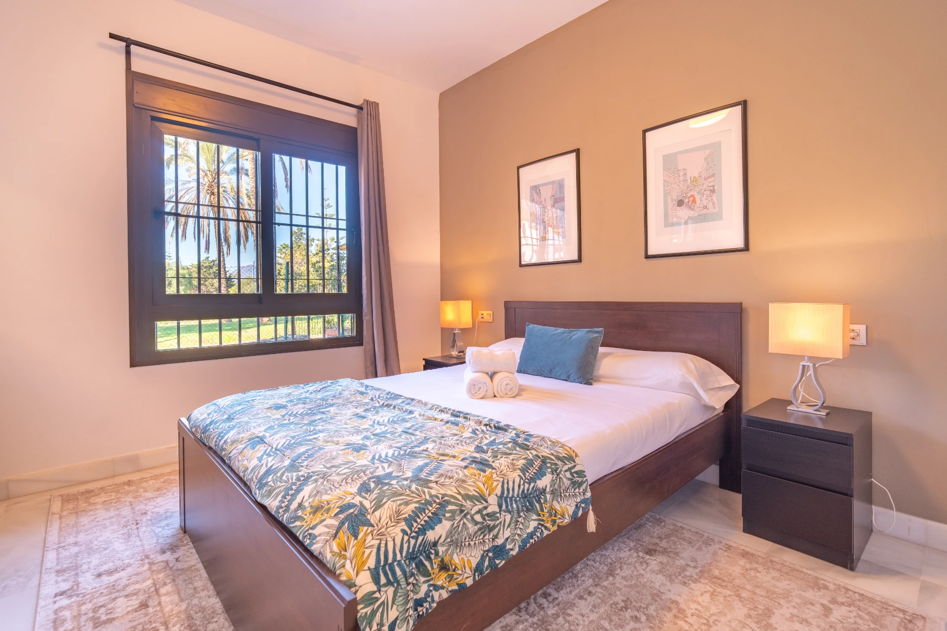 Cozy bedroom with a double bed, decorative bedding, bedside lamp, and window showcasing garden views, reflecting the modern comfort of a vacation rental in Marbella.