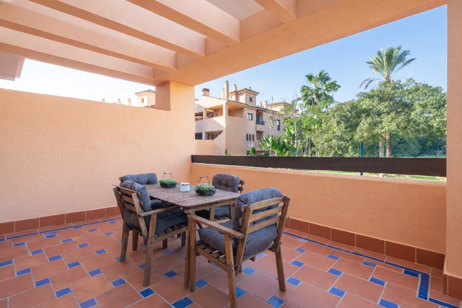 Terrace with wooden dining set, potted plants, and views of gardens and palm trees, ideal for breakfast in a Marbella vacation rental.