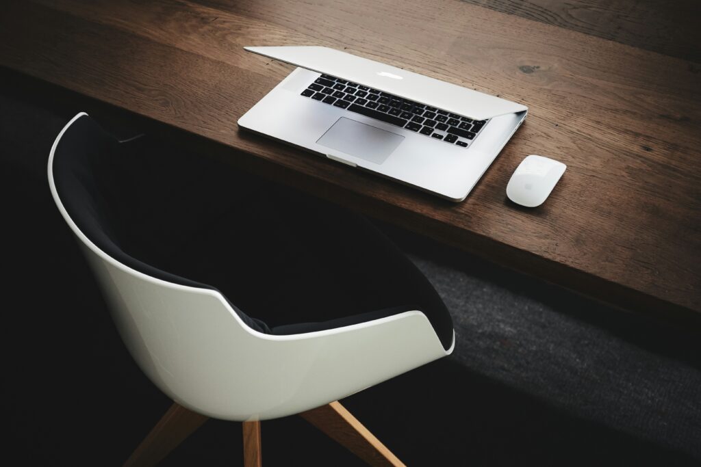 Laptop on wooden desk beside a white mouse, with a modern chair, representing a productive workspace suitable for remote work in Marbella.